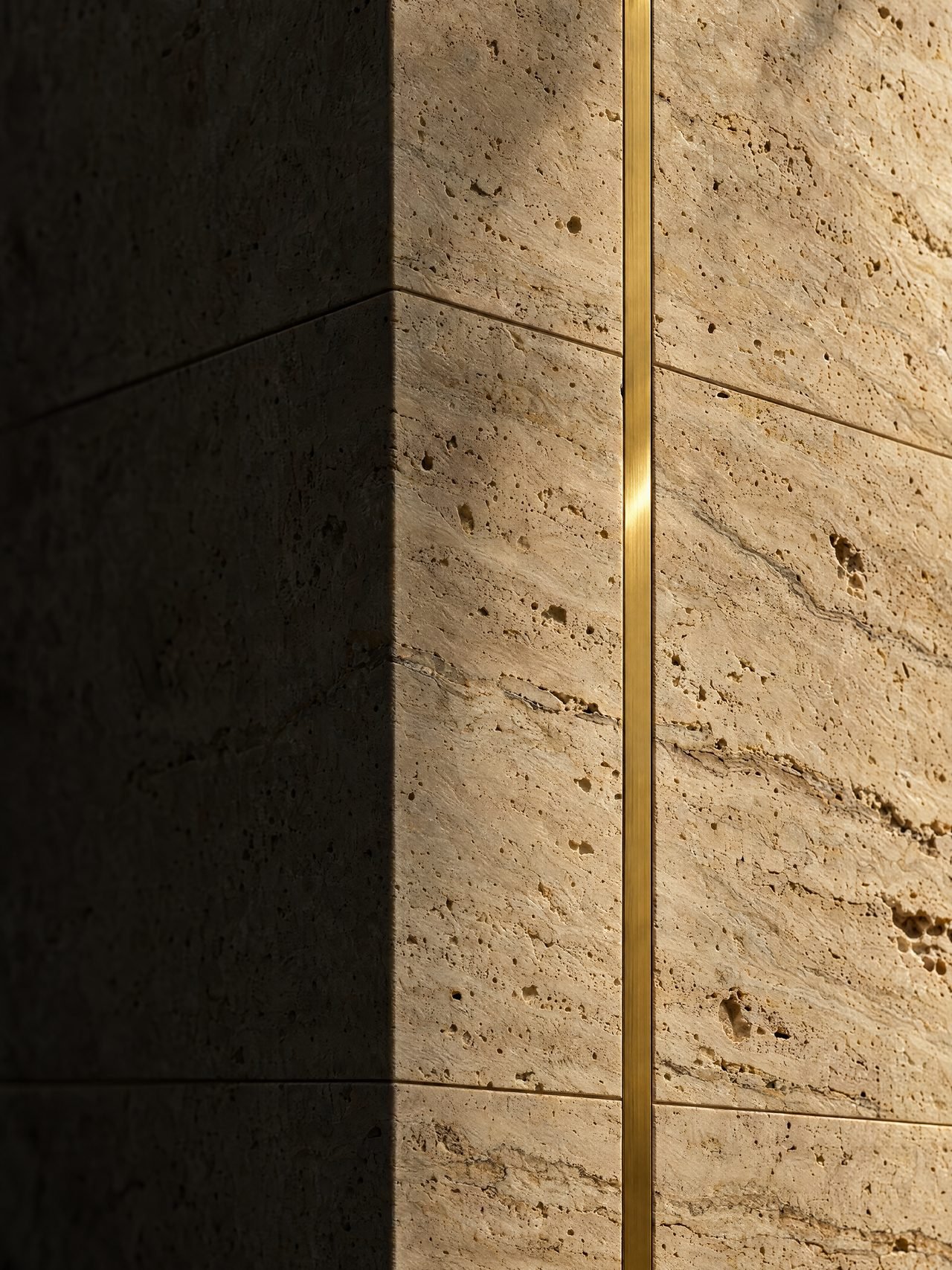 A corner of honed travertine with a single brass inlay line, half in raking sunlight and half in shadow