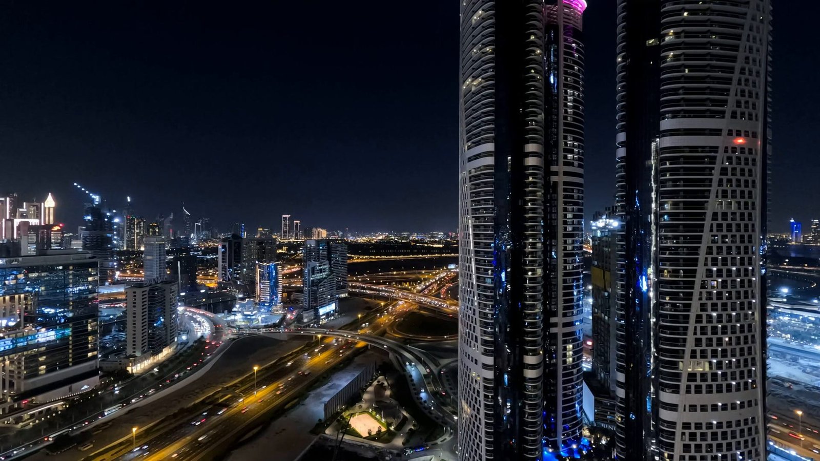 Dubai at night from the air, the towers of Sheikh Zayed Road lit above the traffic